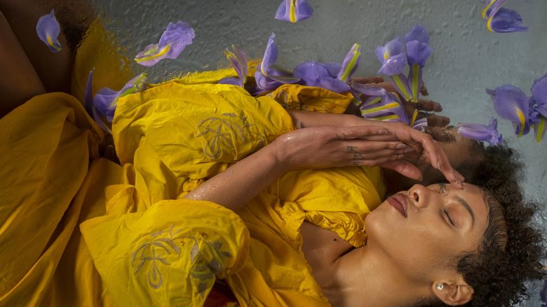 photograph of woman in yellow laying down around purple flowers