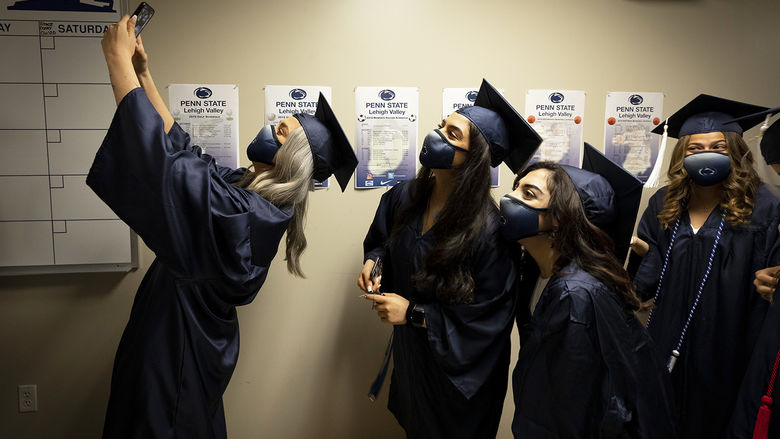 female graduates in cap and gowns take selfie