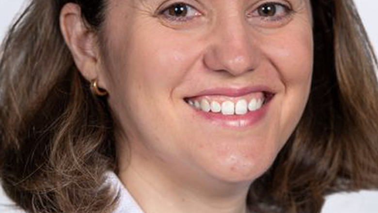 Woman smiling and looking at camera, wearing a white suit jacket.