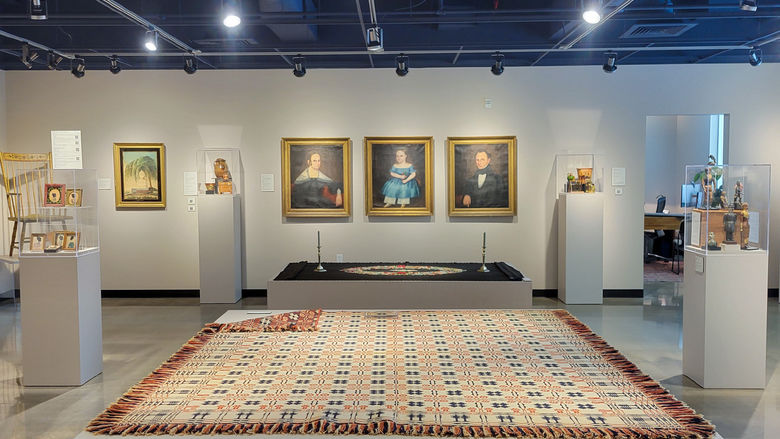 A gallery with classical paintings on the wall and textiles laid out for display throughout the room
