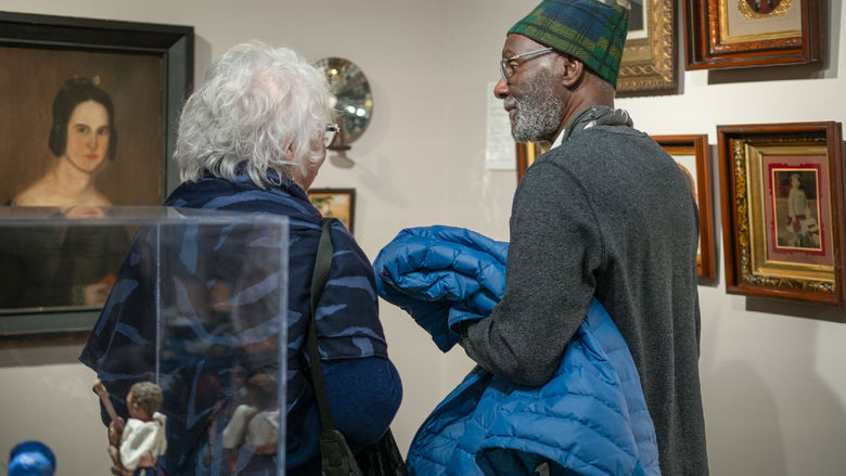 A man and woman stand in the corner of two gallery walls and discuss the works on display