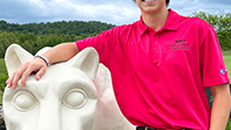 PSU-LV male student in bright pink New Student Orientation leader shirt smiling, standing next to the PSU-LV lion shrine.