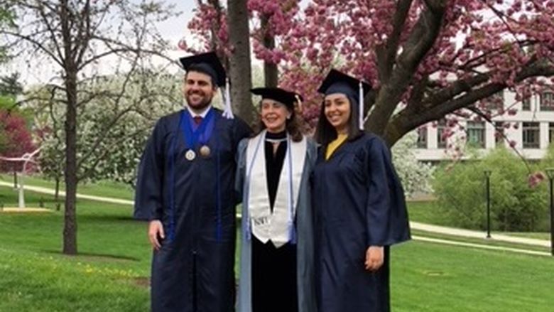 Professor posing with two students under tree in caps and gowns