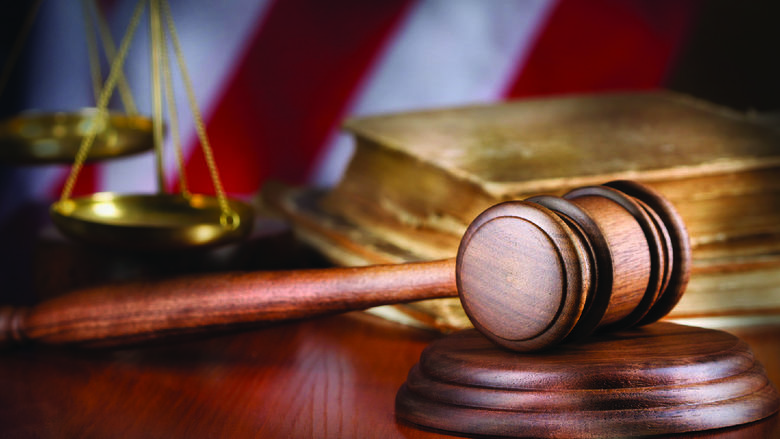 A gavel with the scales of justice, a book and an American flag in the background