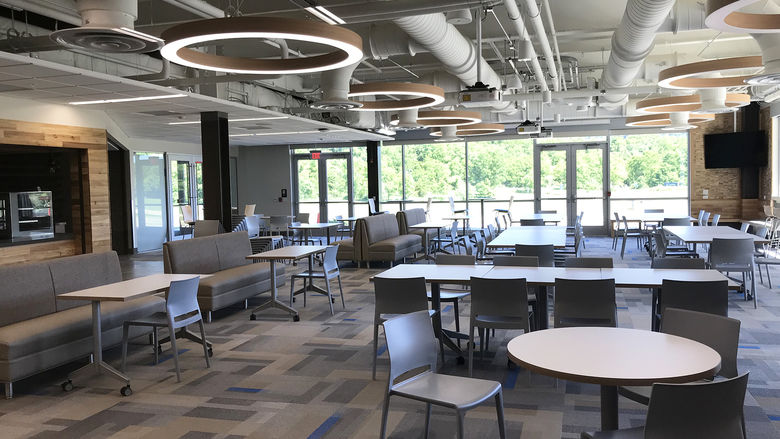 a large room with an exposed ceiling, a wall of windows, and multiple round tables and booths.