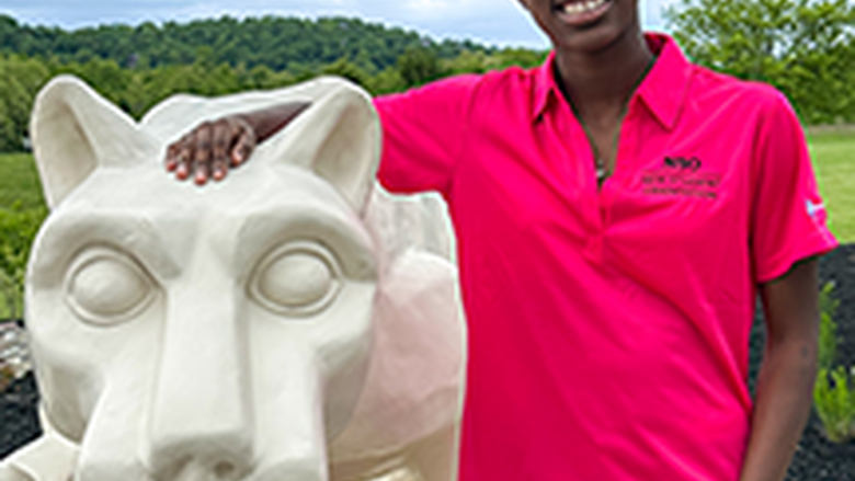 PSU-LV female student in bright pink New Student Orientation leader shirt smiling, standing next to the PSU-LV lion shrine.