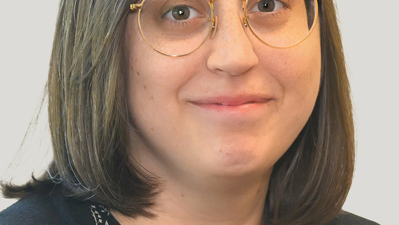 Woman with shoulder length straight brown hair and glasses looks at camera with a slight smile.