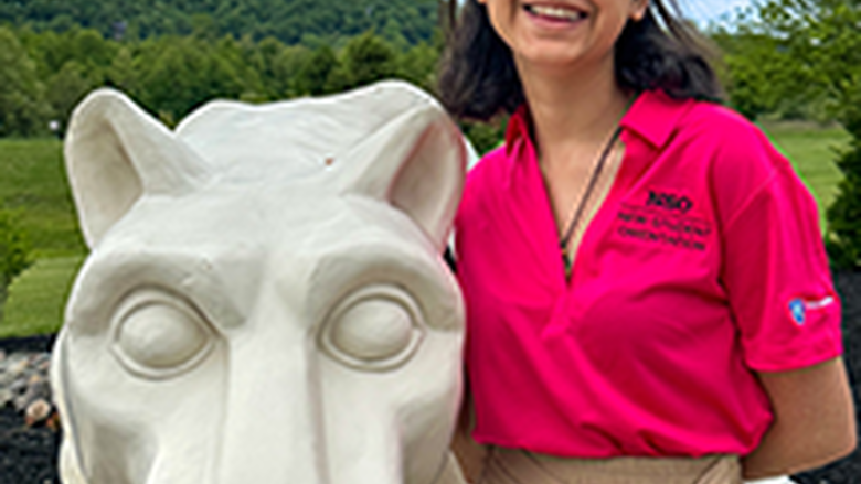 PSU-LV female student in bright pink New Student Orientation leader shirt smiling, standing next to the PSU-LV lion shrine.