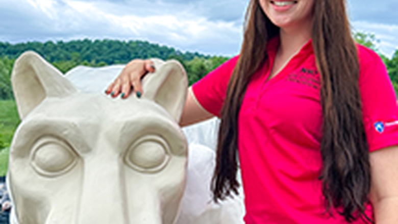 PSU-LV female student in bright pink New Student Orientation leader shirt smiling, standing next to the PSU-LV lion shrine.