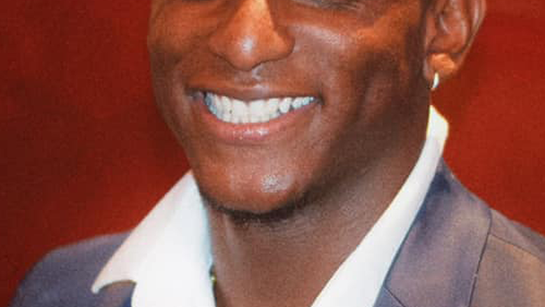 Man smiles and looks at camera, wearing a navy suit jacket and white shirt.
