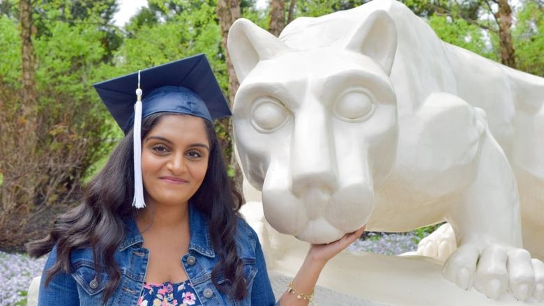 female student in cap and gown at Nittany Lion shrine