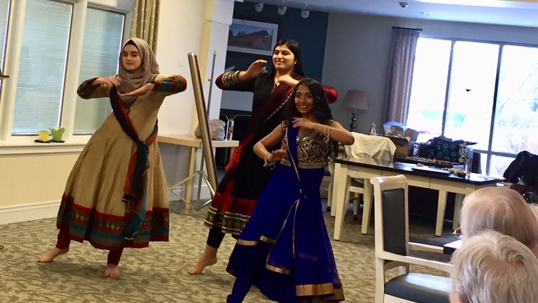 three young women in cultural dress dancing at senior center
