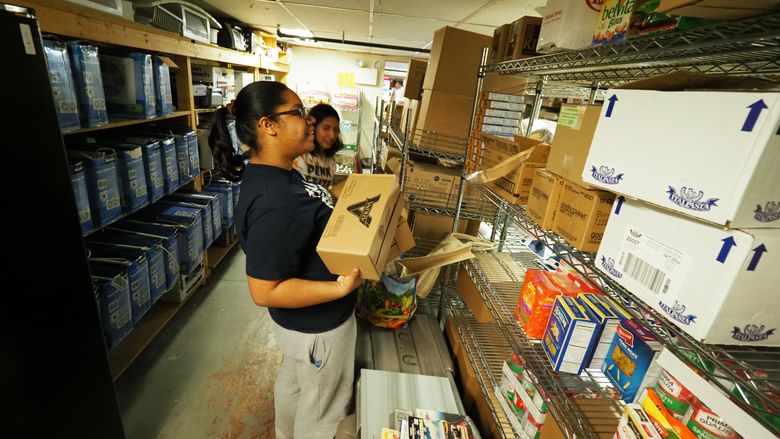 Young woman sorting donations and stacking boxes on shelf
