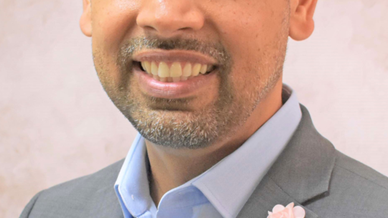 Man wearing a grey suit and light blue shirt smiles at camera.
