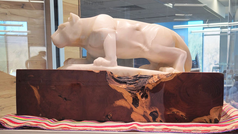 Mountain lion carved from alabaster on a wooden base. Under the base is a colorful woven blanket
