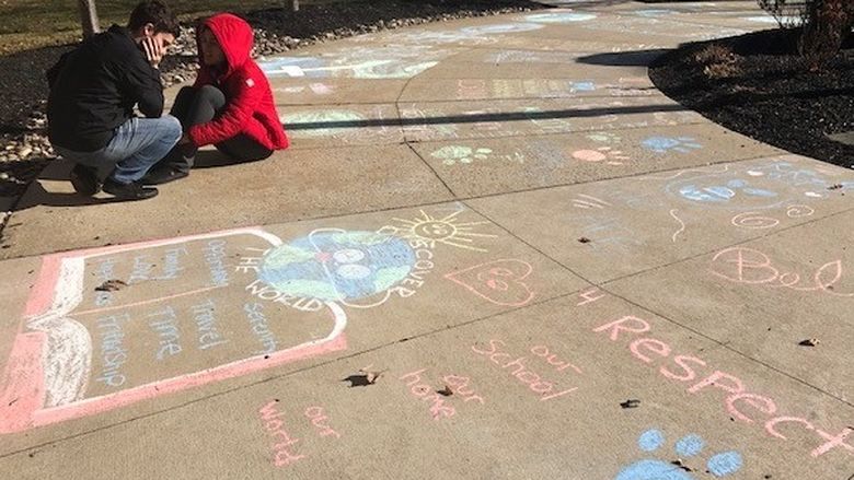 two students sitting on sidewalk with chalk drawings
