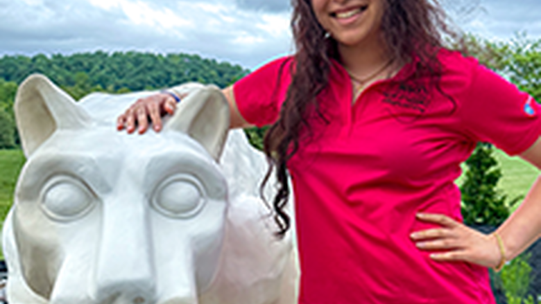 PSU-LV female student in bright pink New Student Orientation leader shirt smiling, standing next to the PSU-LV lion shrine.