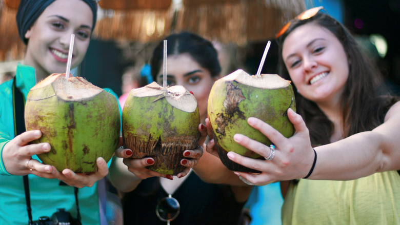 Three young women holding coconut drinks