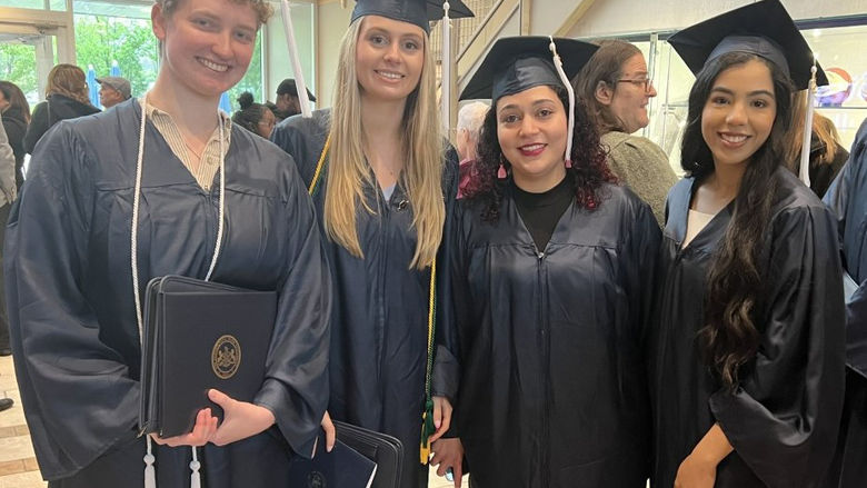 Four graduates wearing caps and gowns pose for picture at a graduation ceremony