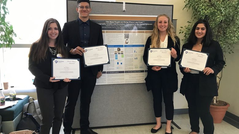Four students posing in front of research poster