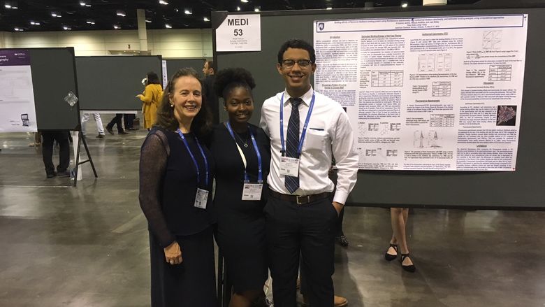 professor and two students in front of research poster