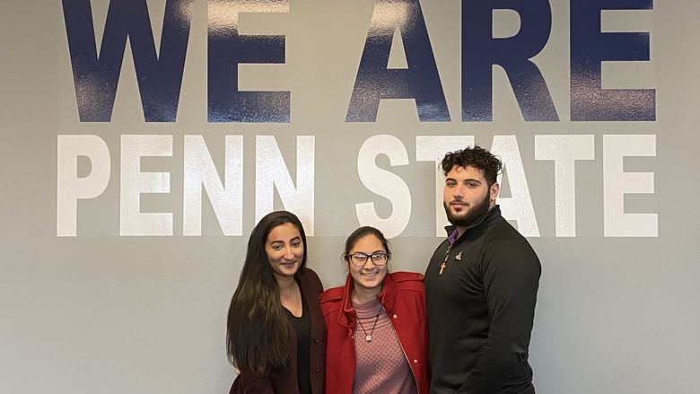 three students in front of a We Are Penn State 