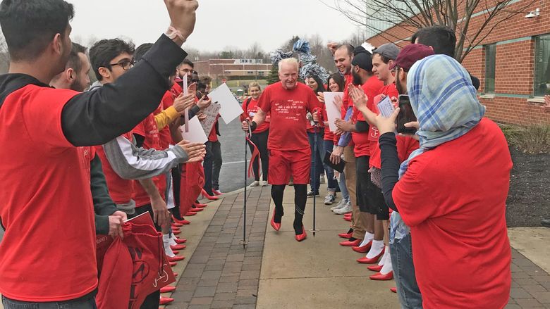 Man using walking sticks in center, as students cheer him on on either side