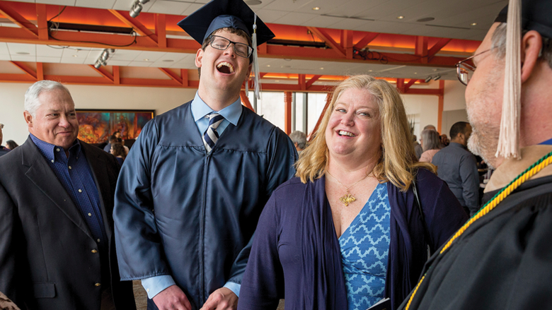 student in graduation cap and gown laughing with family 