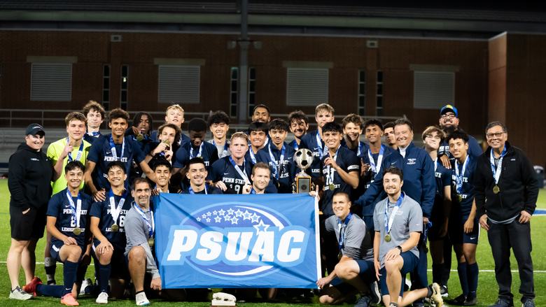 male soccer players pose for a group photo on a soccer field with a blue flag
