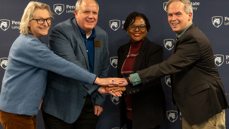 four individuals put their hands in a pile in the middle and smile at the camera 