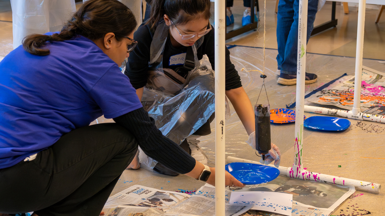 Two people crouch down to examine a science experiment on the floor