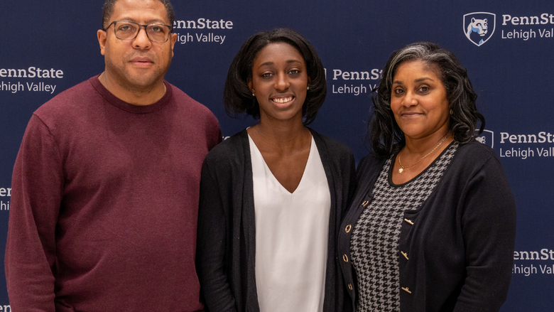 a female student smiles with her parents in front of a Penn State Lehigh Valley backdrop