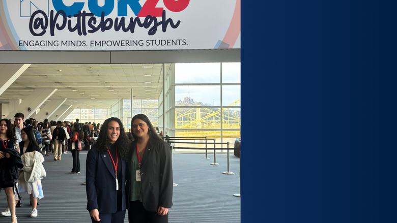 two female students smile in front of a conference banner