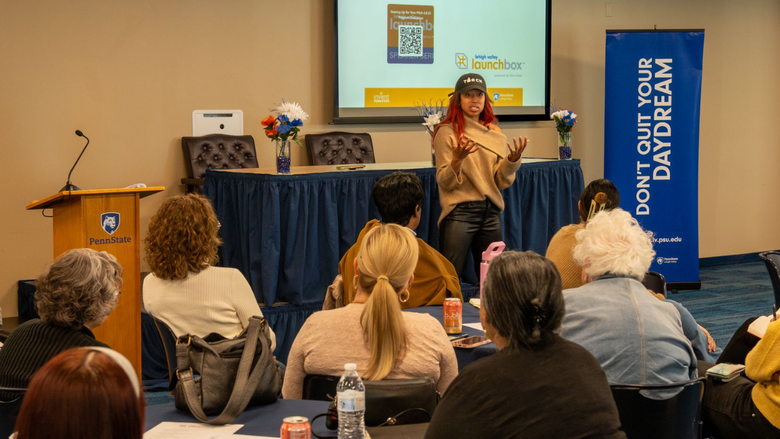 a woman speaks in front of an audience seated at round tables