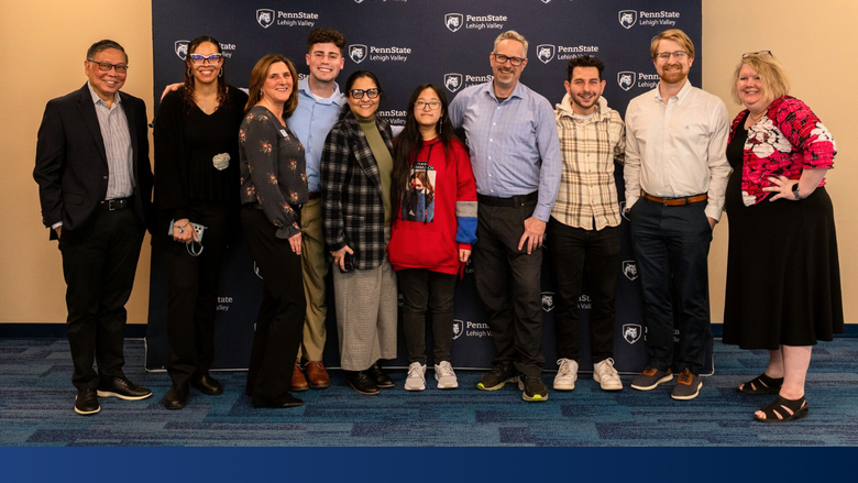 a group of faculty and staff smile in front of a Penn State backdrop