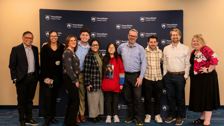 a group of faculty and staff smile in front of a Penn State backdrop