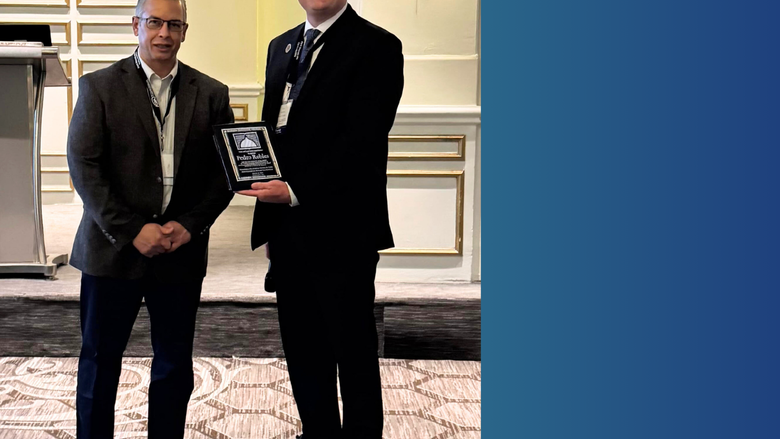Two people stand next to each other. One holds an award. 