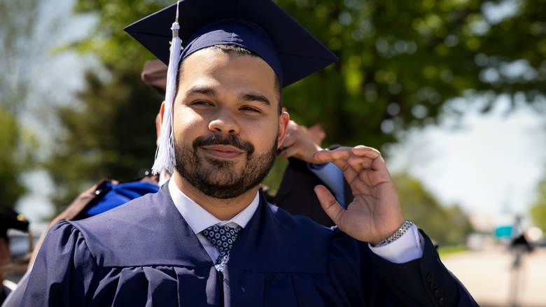 a male student in blue regalia smiles as he prepares to process in a commencement ceremony