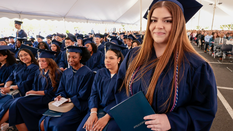 A woman in blue regalia smiles as she holds her blue Penn State Lehigh Valley diploma