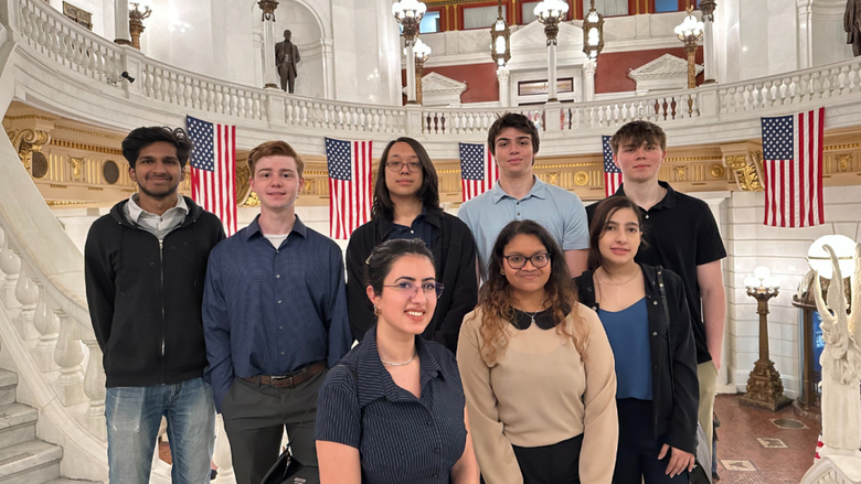 Eight people smile on the steps inside the Capitol Building in Harrisburg 