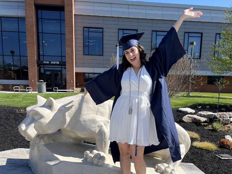 New Penn State graduate Anna Raffeinner celebrates with a joyful expression with the Lion Shrine on the Penn State DuBois campus, just outside the PAW Center