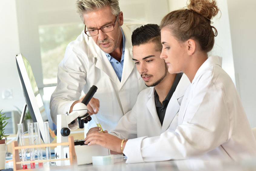 Three people in lab coats at microscope