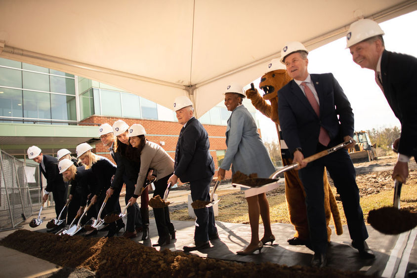 twelve people with shovels in hand turn over dirt