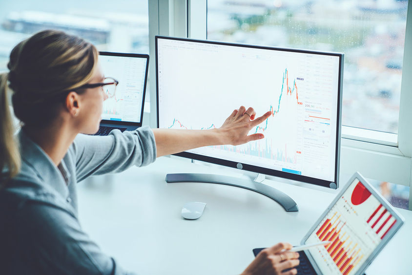 woman pointing to computer screen and tablet featuring bars and graphs