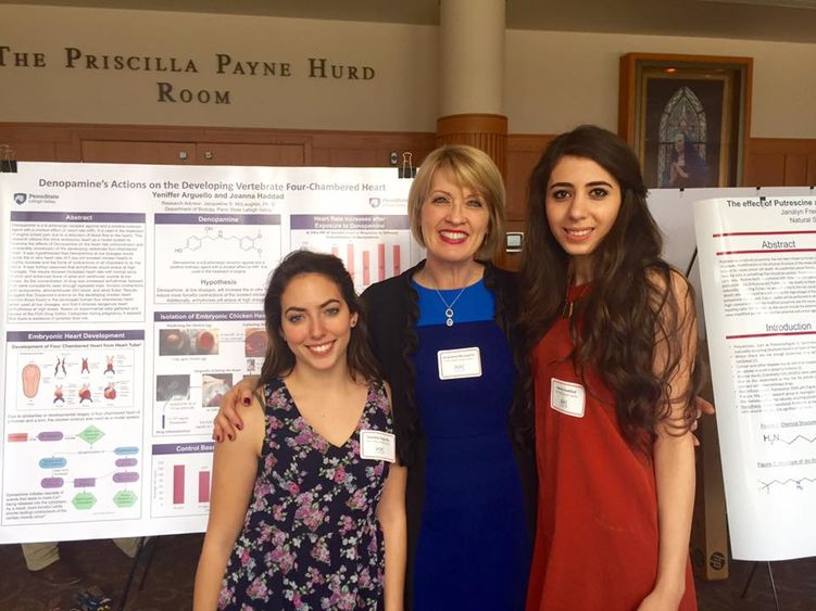 Two students pose with professor in front of their research project Two students pose with professor in front of their research project
