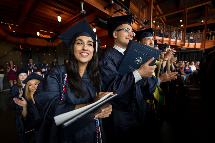 several students standing in clapping in caps and gowns