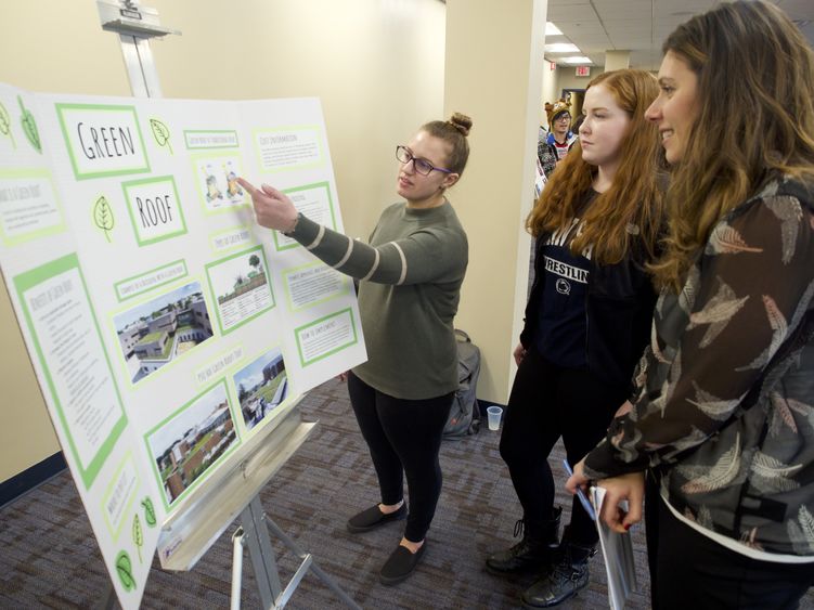 student pointing to a poster showing her research to bystanders