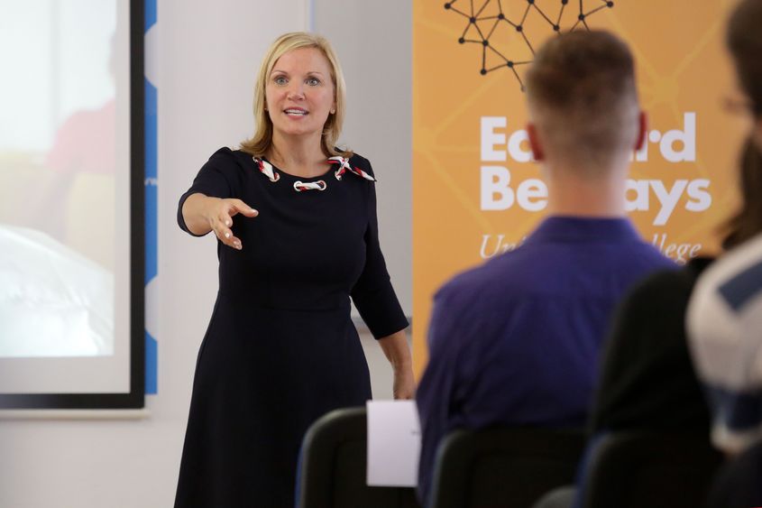 woman gesturing while speaking to a class of students