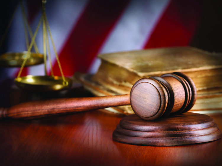 A gavel with the scales of justice, a book and an American flag in the background