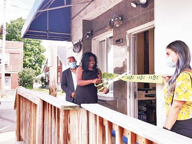 people wearing masks outside a storefront cutting a yellow ribbon